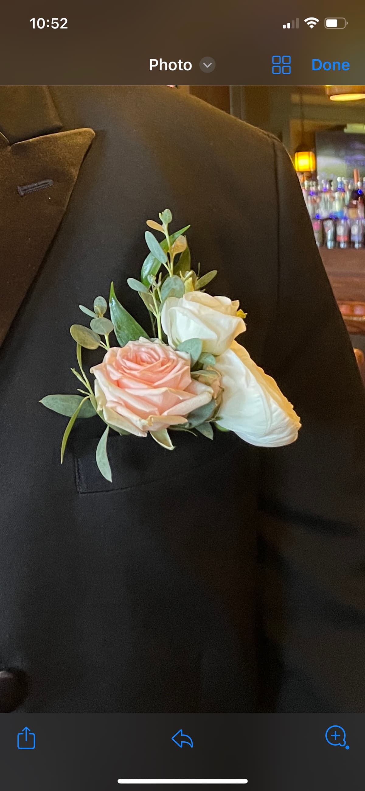Close-up of a floral pocket square arrangement tucked into a black tuxedo jacket pocket, featuring a blush pink rose, white blooms, and sprigs of eucalyptus greenery.